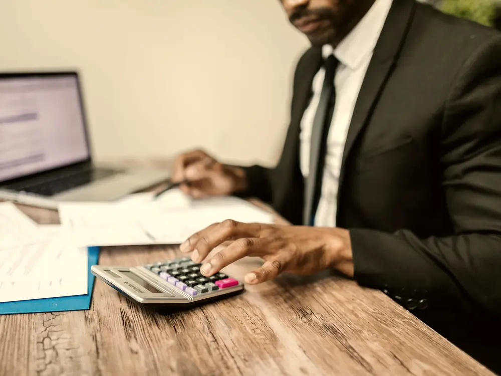 Accountant using a calculator beside a laptop and financial documents