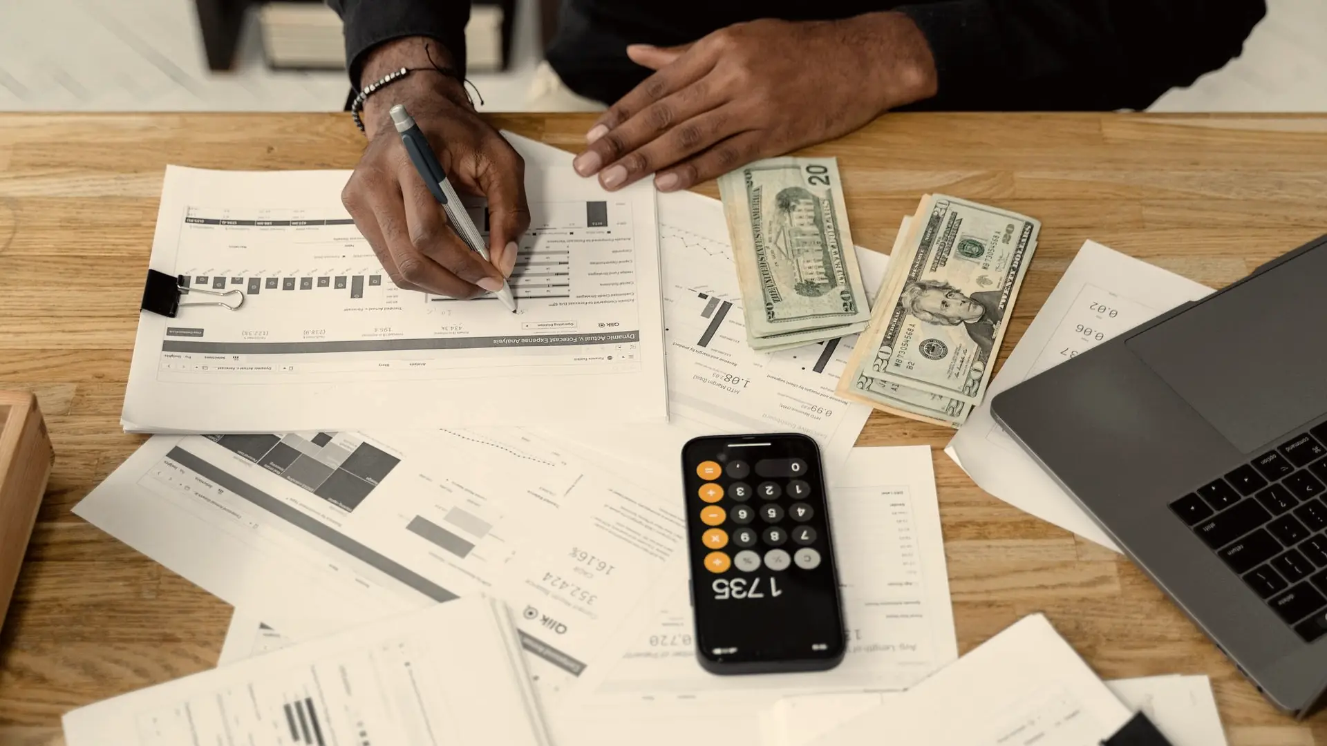 Accountant working through financial reports with a calculator, cash and a laptop