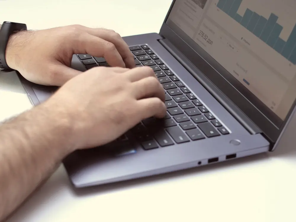 Hands typing on a laptop that shows analytics charts