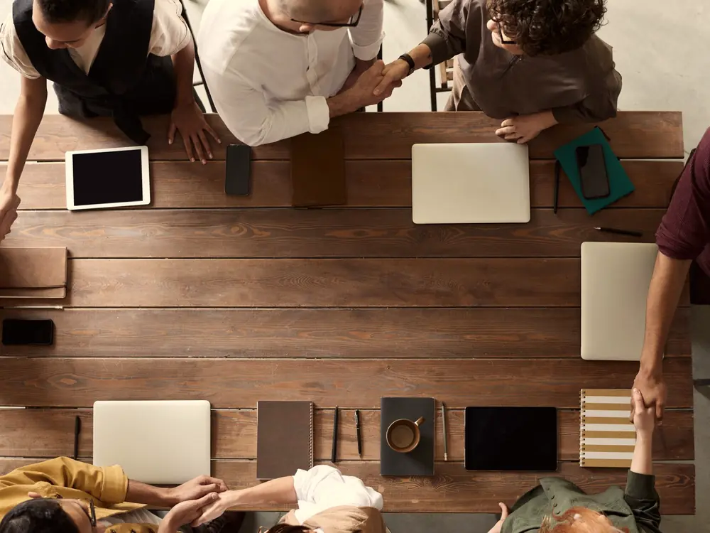 Overhead view of a team meeting around a wooden table with laptops and tablets