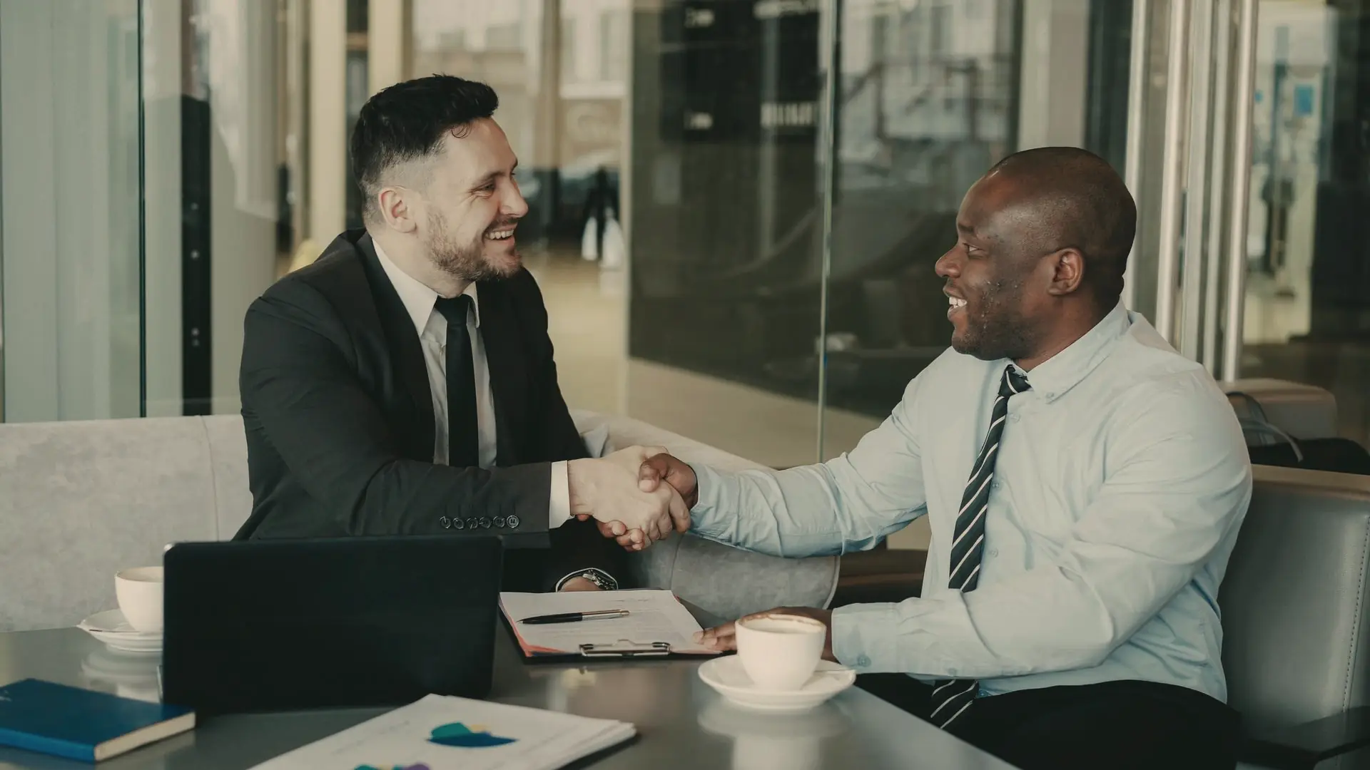 Two businessmen shaking hands over a deal in a hotel lounge meeting area